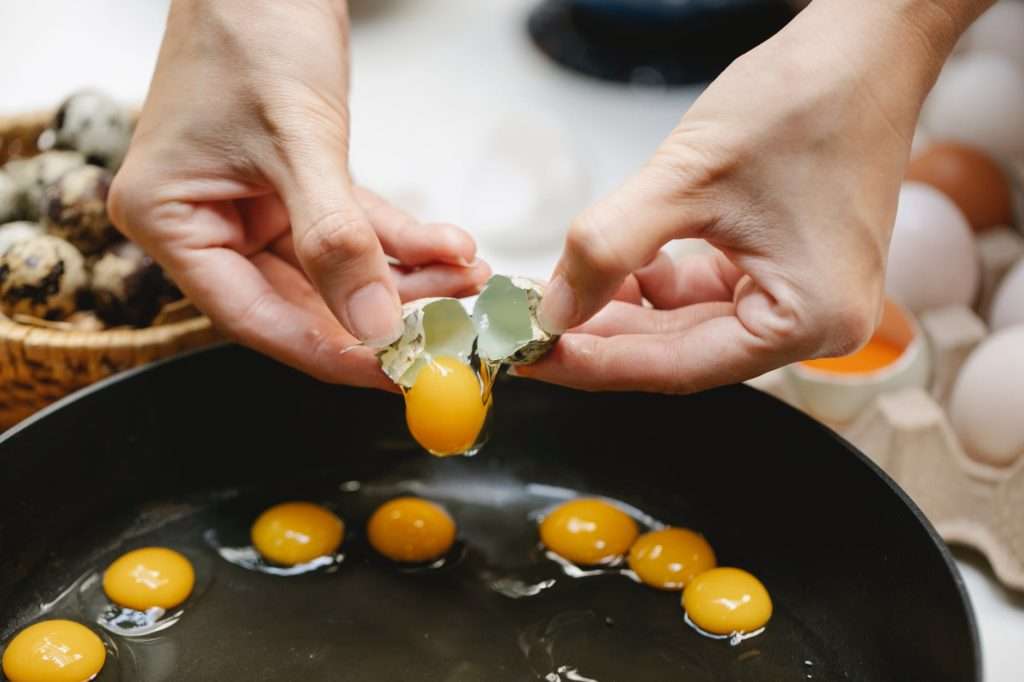 crop cook breaking quail egg into frying pan